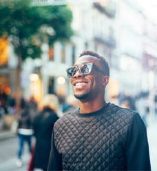 a smiling person wearing sunglasses walking down a busy street