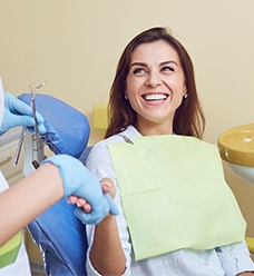 smiling woman in dentist chair shaking hands