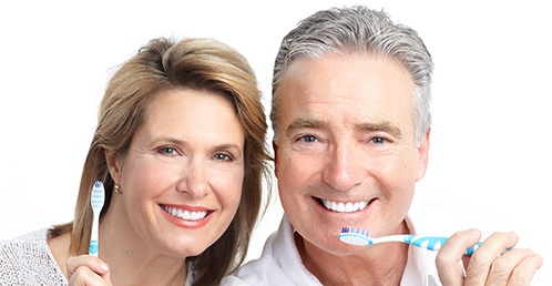 An older couple holding toothbrushes and smiling