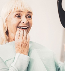 A woman admiring her dentures in a hand mirror