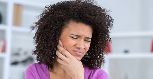 A young woman wearing a purple blouse and holding her jaw in pain waiting to see an emergency dentist in Jacksonville