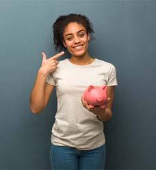 Smiling woman with piggy bank representing cost of dental emergencies in Jacksonville