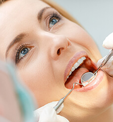 A woman opens her mouth to let her dentist check her restorations during an appointment