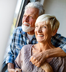 An older couple stare out the window and smile after receiving dental implants