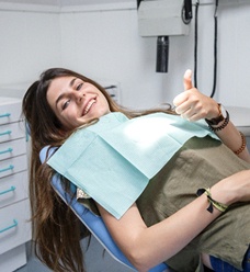 Woman smiling with thumb up while sitting in dental chair