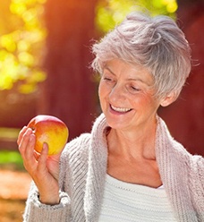 Woman with dental implants in Jacksonville holding an apple
