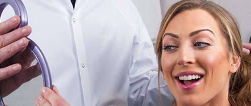 Woman in dental chair looking at her smile in mirror