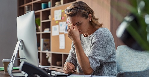 woman tiredly rubbing her eyes at a desk