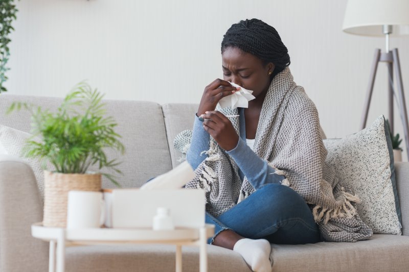 a woman sitting on a couch blowing her nose and looking at a thermometer 