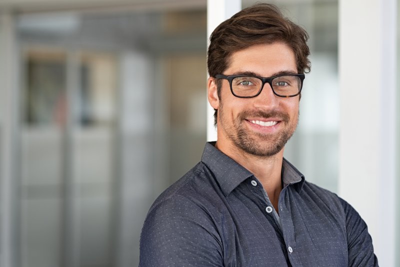 a young man with glasses smiling to show his custom-made dental restorations