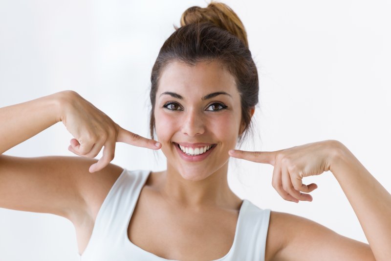 a young woman in a white tank top pointing to her healthy smile