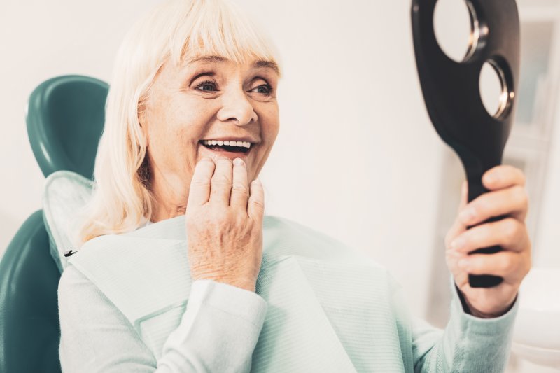 An older woman looking at her dentures in the mirror at the dentist’s office