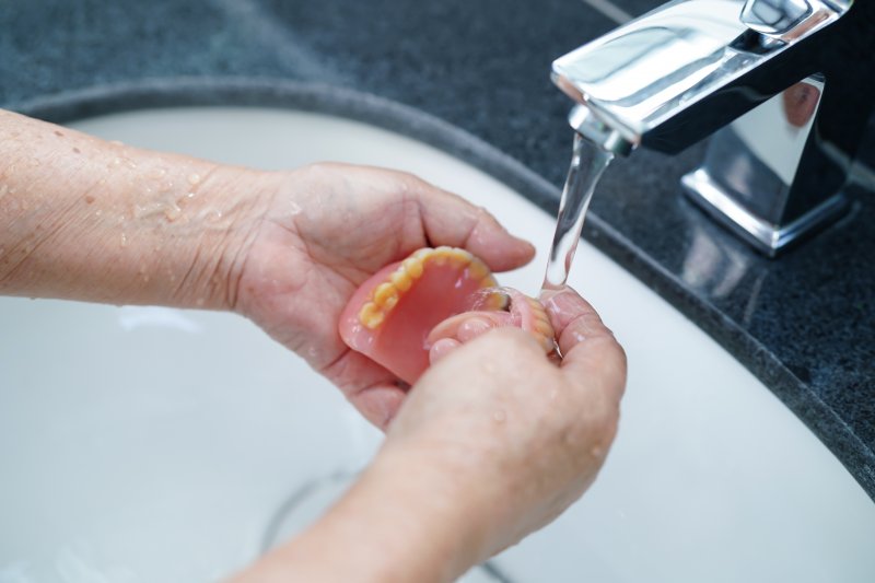 a person cleaning their dentures under a faucet 