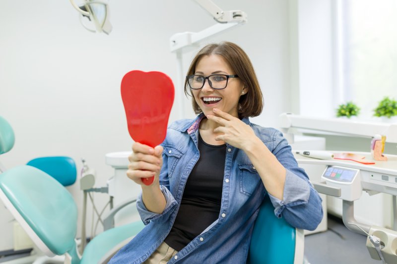 a middle-aged woman looking at her new smile in the mirror after receiving dental implants