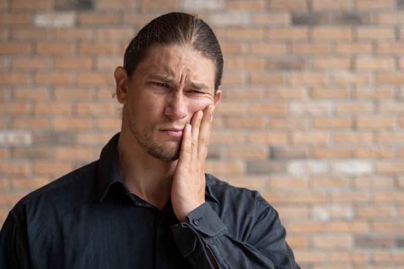 a man wearing a black button-down shirt and holding his cheek in pain because of tooth decay