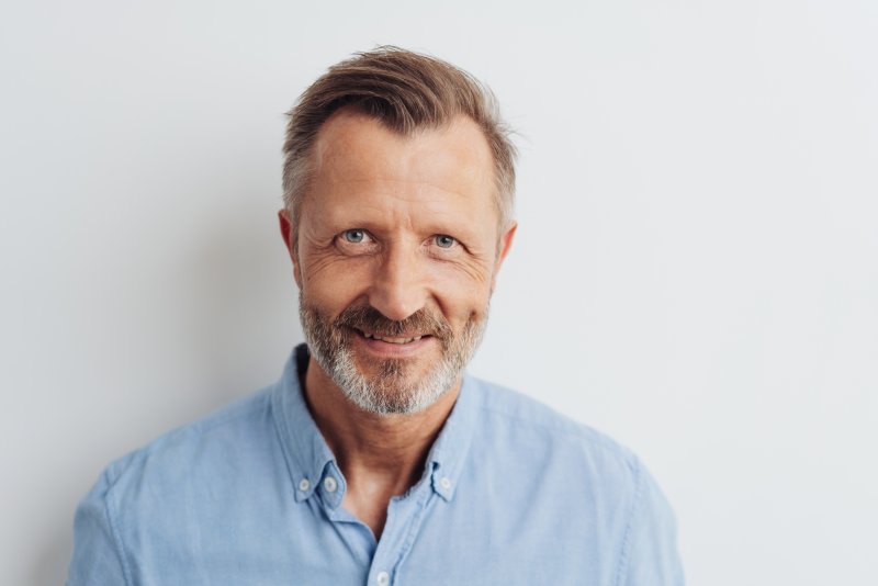 a middle-aged man with a salt and pepper beard wearing a button-down shirt and smiling