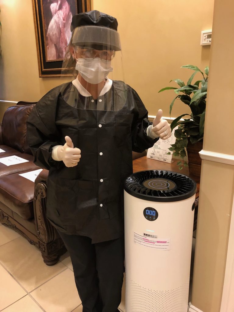 a dental professional giving a thumbs up while standing next to an air purifier