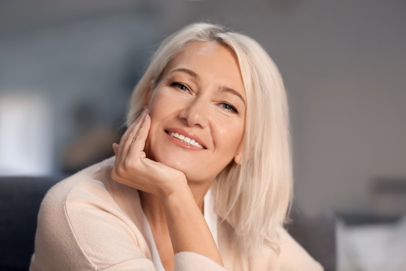 a middle-aged, blonde woman holding her head up with her hand and smiling 