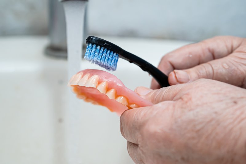 a person holding and cleaning their dentures using a soft-bristled toothbrush