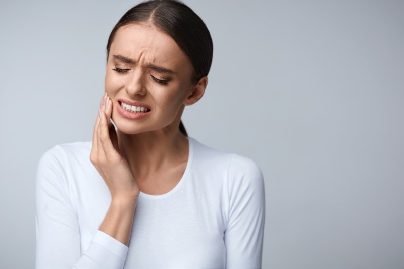 a young woman holding her cheek in pain due to a toothache