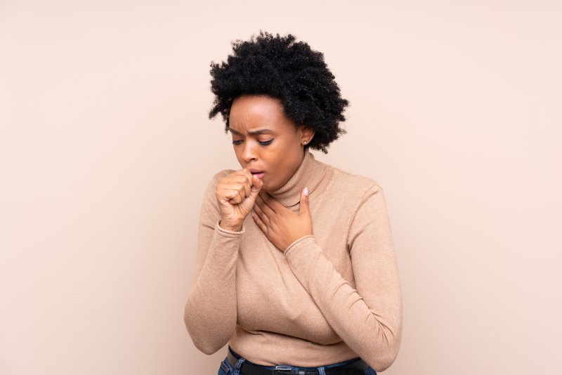 a young woman wearing a cream blouse and coughing into her hand 