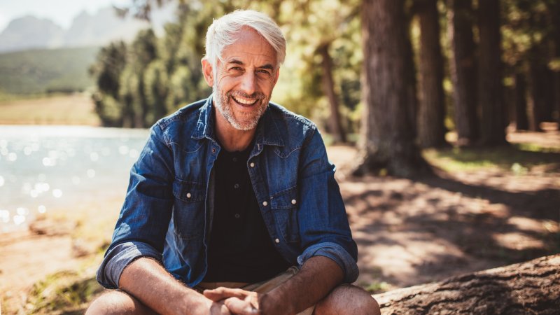 an older man seated outside near a lake and showing off his fully restored smile