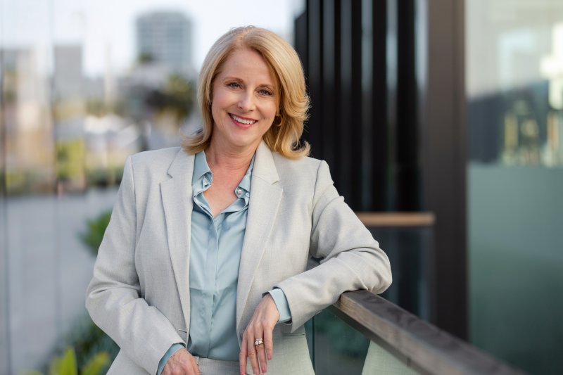 a middle-aged woman wearing a suit jacket and leaning against a railing while smiling