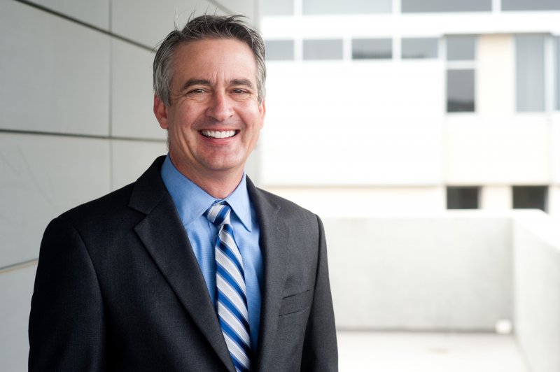 a middle-aged man wearing a suit and tie smiles after receiving his dental implants