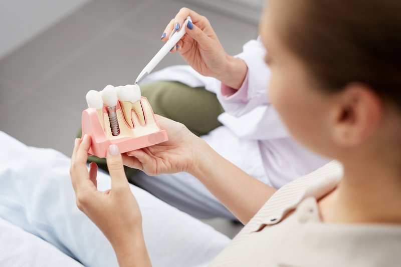 an up-close view of a patient holding a cross-section of a mouth mold that contains a dental implant while a dentist explains how it works