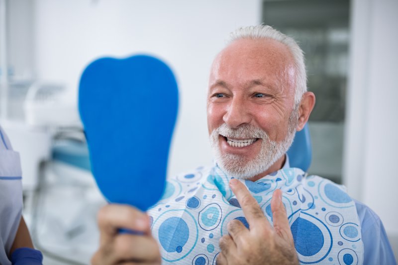 an older man admiring his new smile in the mirror after receiving dental implants