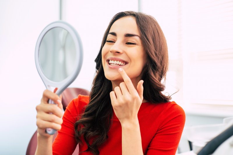 a young woman looking at her new and improved smile in the mirror while at the dentist’s office