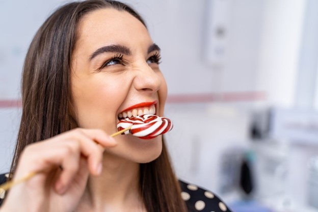 Woman biting into a hard lollipop using her teeth.