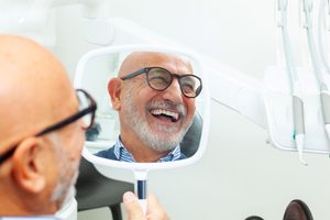 Reflection of smiling bald man in dental chair holding mirror